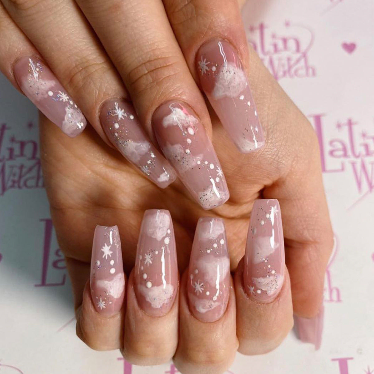 Wearing Nails design featuring long false nails with pink base and white snowflake patterns.